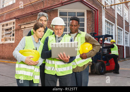 Raccoglitori e gli addetti al magazzino team con il computer portatile nella parte anteriore del magazzino Foto Stock