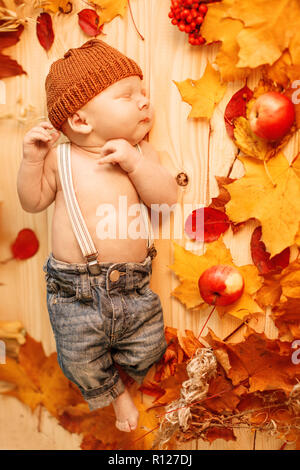 In autunno il neonato. Tempo di autunno scena. piccolo bambino con rosso giallo foglie di acero, bacche, zucca, mele, raccolto. Foto Stock