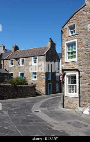 Vecchie case di pietra arenaria in Stromness, Orkney con pietre per pavimentazione da una cava locale e ciottoli nel centro della strada. Foto Stock