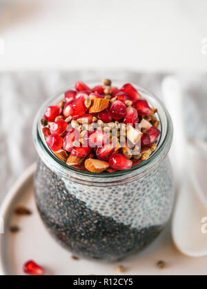 Colazione salutare concetto e idea - due colori chia pudding con materie organiche melograno, mandorla e grani di canapa. Il vasetto di vetro con il nero antracite e bianco latte vegano budino di Chia. Copia dello spazio. In verticale Foto Stock