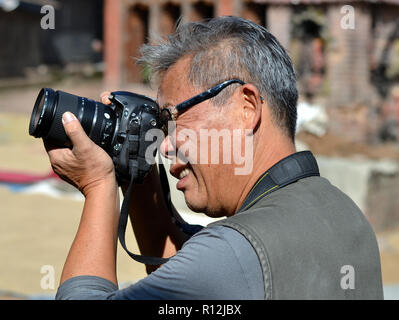 Di mezza età maschio cinese street fotografo prende la mira con la sua Nikon fotocamera reflex digitale. Foto Stock