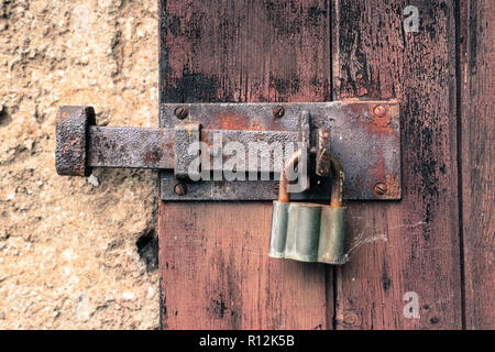 Chiuso il vecchio di ferro arrugginito e blocco lucchetto vintage sul cracking e spellatura weathered red porta di legno. Foto Stock