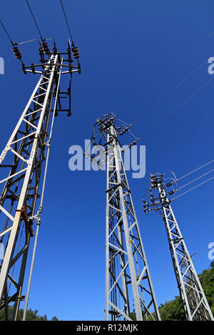 Torri di elettricità nei pressi di una diga contro la montagna di profondo cielo blu Foto Stock