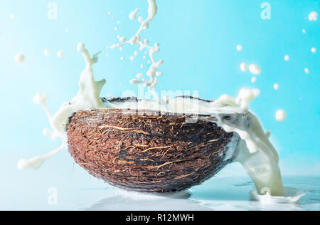 Noce di cocco con il latte splash su uno sfondo blu, gli spruzzi di latte di cocco Foto Stock