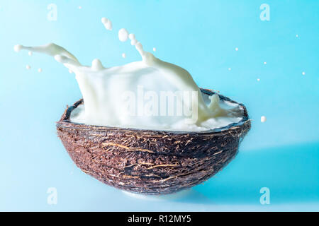 Noce di cocco con il latte splash su uno sfondo blu, gli spruzzi di latte di cocco Foto Stock