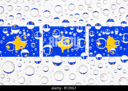 Le bandiere del Kosovo dietro un vetro ricoperto di gocce di pioggia. 3D illustrazione Foto Stock
