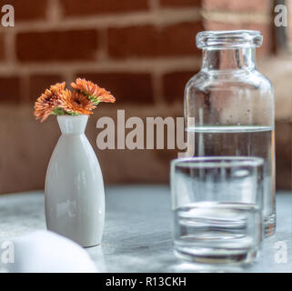 Casual caffetteria. Latte art. La formazione di schiuma del latte. Brocca in vetro chiaro. Fiori d'arancio in un bianco ovale vaso bianco. Foto Stock