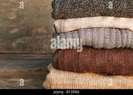 Pila di coloratissimi vestiti caldi su sfondo di legno. Foto Stock