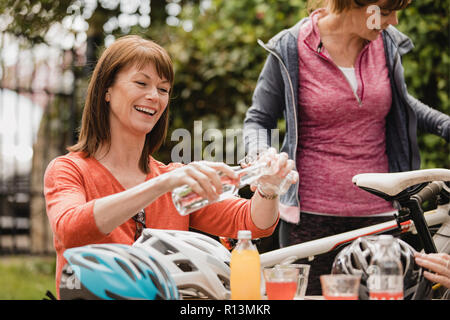 Piccolo gruppo di femmina matura ciclisti seduto fuori area con posti a sedere di un cafe'. Tey sono godendo di alcune bevande come si prendono una pausa. Foto Stock