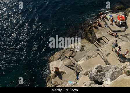 Dubrovnik Città Vecchia i turisti a prendere il sole sulle rocce sotto le antiche mura della città Foto Stock