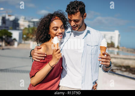 Matura in amore a camminare su una strada di città di mangiare gelati. Giovane uomo e donna di trascorrere del tempo insieme a camminare sulla strada a parlare e a mangiare il gelato. Foto Stock