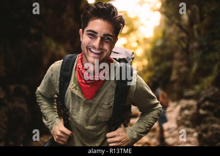 Ritratto di felice giovane con uno zaino trekking in montagna con gli amici sul retro. Uomo che guarda la fotocamera e sorridente durante le escursioni nella natura. Foto Stock