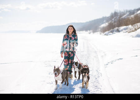 Donna allegra proprietario a piedi con i suoi cani all'aperto sulla neve nella soleggiata giornata invernale. Foto Stock