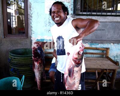 BINANGONAN, Rizal, Filippine - 8 Novembre 2018: un pesce porta e lavoratore del mercato mette in mostra un paio di grandi pesci pronti per la vendita. Foto Stock