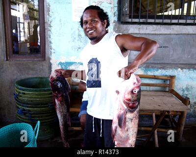 BINANGONAN, Rizal, Filippine - 8 Novembre 2018: un pesce porta e lavoratore del mercato mette in mostra un paio di grandi pesci pronti per la vendita. Foto Stock