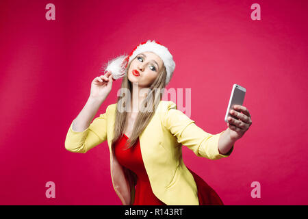 La donna sorpresa in santa hat rendendo selfie su sfondo rosa. Foto Stock