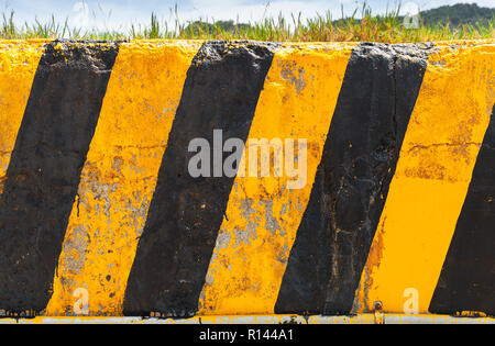 Rigato nero giallo attenzione pattern su una schifezza blocco di calcestruzzo su una strada in giorno di estate Foto Stock