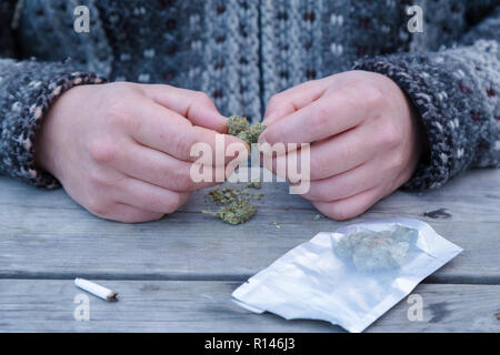 Close-up di un mans mani rompendo la marijuana gemme accanto a un dispensario sacco e un giunto. Foto Stock