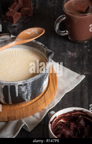 Ingredienti per la cioccolata calda contesto, con il latte in una casseruola rustico, cioccolato e cacao e una tazza di cioccolata calda, su una tavola nera. Foto Stock