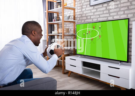 African giovane uomo gettando calcio in televisione a casa Foto Stock