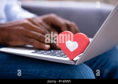 Close-up di Heartshape rossa sulla tastiera mentre la mano d'uomo utilizzando Laptop Foto Stock