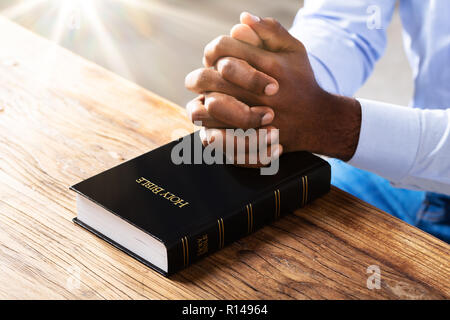 Close-up di un uomo di preghiera Mani sulla Bibbia libro sulla scrivania in legno Foto Stock