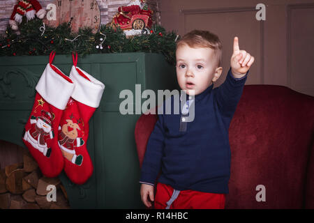 Ragazzo Litlittle sollevando il dito vicino a sfondo di Natale Foto Stock