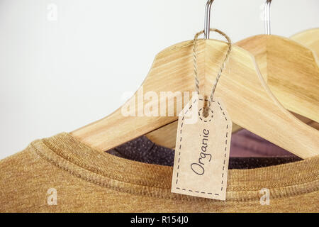 Abbigliamento organico. Colore naturale t-shirts appesi i portabiti in legno in una fila. Foto Stock