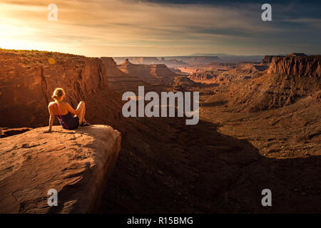 Escursionista ragazza ammira Sunrise a forcella est Shafer Canyon nei pressi di Dead Horse Point State Park Canyonlands Utah STATI UNITI D'AMERICA Foto Stock