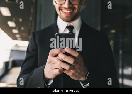 Immagine ritagliata di bello uomo d affari vicino al centro business utilizzando il telefono cellulare. Foto Stock