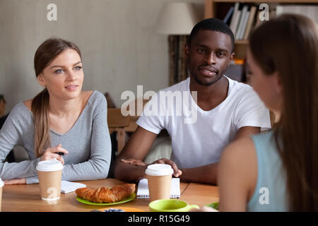 Ragazze caucasico africano nero ragazzo a parlare avente una piacevole conversazione a pranzo, caffè e croissant sul tavolo. Diversi gli studenti che studiano insieme mak Foto Stock