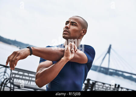 Un close-up ritratto di un africano uomo fitness stretching mani su una banchina sfondo al parco. Foto Stock