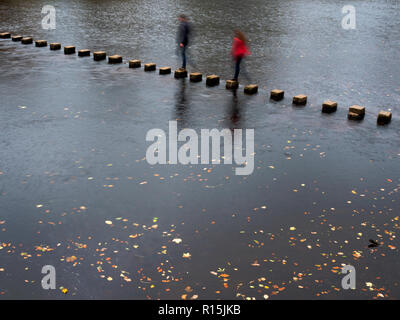 Due figure sfocate attraversando le pietre miliari sul fiume Wharfe in autunno a Bolton Abbey Yorkshire Dales Inghilterra Foto Stock