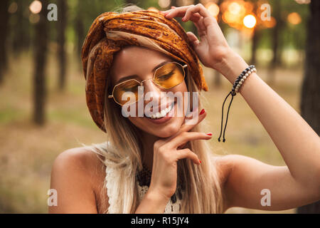 Foto di gioiosa hippie donna che indossa gli eleganti accessori sorridere mentre passeggiate in foresta Foto Stock