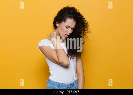 Immagine della donna stanchi 20s con capelli ricci di toccare e massaggiare il collo isolate su sfondo giallo Foto Stock