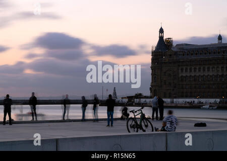 Istanbul, Turchia - 4 Novembre 2018: alcune persone stanno prendendo foto vicino al mare al Kadikoy al tramonto del tempo. Un uomo è seduto accanto alla sua Salcano. Foto Stock