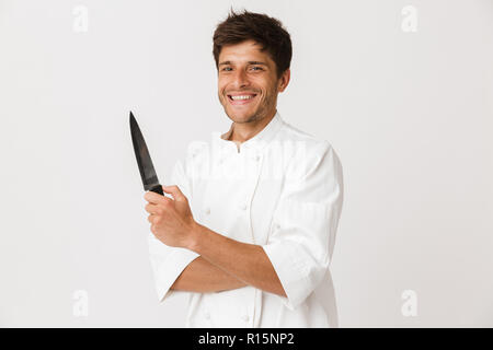 Immagine del bel giovane chef man standing isolate su muro bianco sullo sfondo tenendo il coltello. Foto Stock
