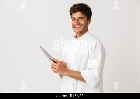 Immagine del bel giovane chef man standing isolate su muro bianco sullo sfondo tenendo il coltello. Foto Stock