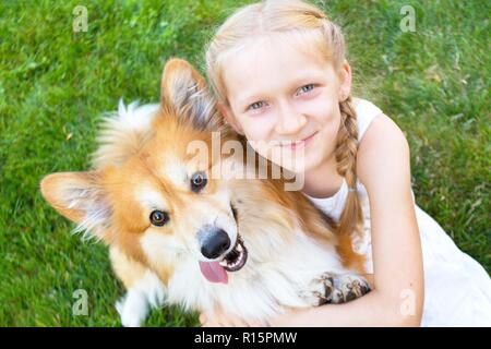 Divertimento bella ragazza bionda e corgi fluffy sorriso e guardare la fotocamera sul prato su una soleggiata giornata estiva Foto Stock