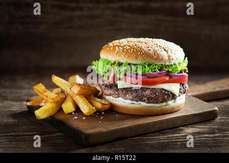Deliziosi hamburger con formaggio e patatine fritte sul tavolo di legno e uno sfondo scuro Foto Stock