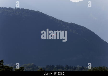 Parapendio in volo la mattina presto nebbie in tra le montagne sopra il lago di Annecy Francia Foto Stock