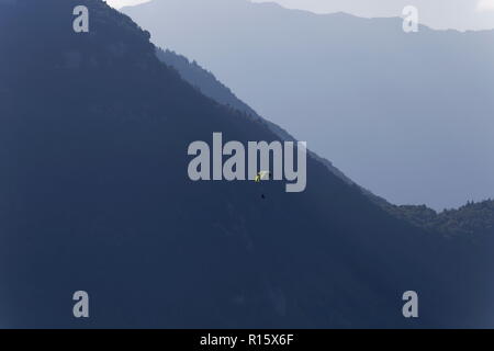Parapendio in volo la mattina presto nebbie in tra le montagne sopra il lago di Annecy Francia Foto Stock