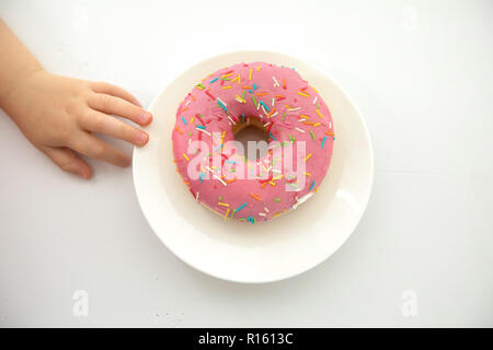 Ritagliare la mano del bambino vicino a ciambella Foto Stock