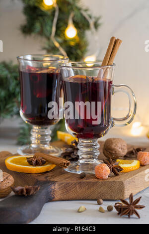 Composizione d'inverno. Vin brulé in bicchieri sul pannello di legno a sfondo bianco. Ghirlanda di abete, arancio cannella e spezie vicino a. Foto Stock