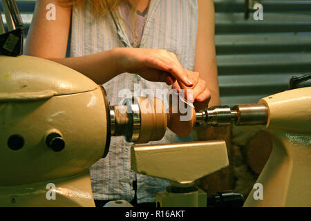 Una giovane donna usando carta vetrata a sua volta una ciotola di legno su un tornio Foto Stock