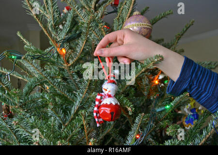 In prossimità di una giovane donna di mano e braccio come lei decora un albero di Natale con un pupazzo di neve felice ornamento Foto Stock