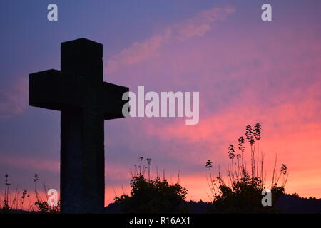 Time-lapse del sole al tramonto di sera Cielo di tramonto visto da dietro una pietra arenaria rossa croce durante l'impostazione di Sun nel cimitero civile Reimsbach Foto Stock