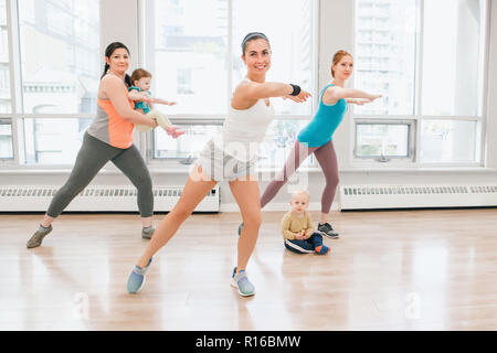 Un gruppo di tre giovani donne con bambini a fare allenamento in palestra di classe con istruttore per perdere il peso del bambino. Bambino-friendly di idoneità per le mamme con bambini Foto Stock