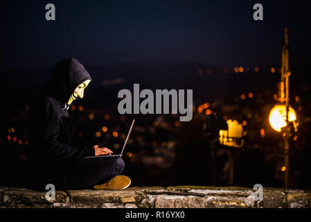 Trieste, 08 novembre 2018. Una persona indifinited con Anonimus maschera e notebook in strada notte. Concetto di sicurezza informatica Foto Stock