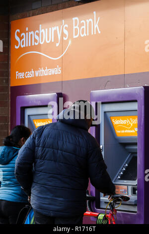 Ci sono due persone che si utilizza la macchina in contanti a Sainsbury's supermercato a Londra. I supermercati e i negozi di comodità non avrà più a pagare milioni di sterline di tariffe business per le macchine di contanti al di fuori dei loro negozi, a seguito di una sentenza della Corte di Appello. Dal 2010 i supermercati e i negozi di comodità sono state soggette al pagamento di tariffe su macchine e la corte di appello ha deliberato che circa £300m è già stata caricata e ora dovranno essere rimborsati. I negozi che sarà immediatamente vantaggio comprendono Sainsburys e Tesco, che aveva preso il caso in appello. Foto Stock